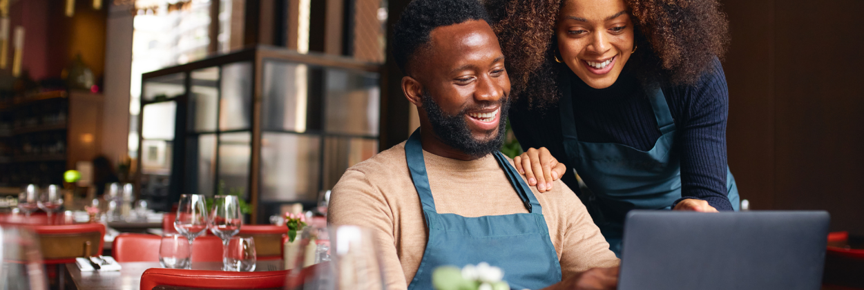 restaurant employees smiling while inside a restaurant looking at a laptop